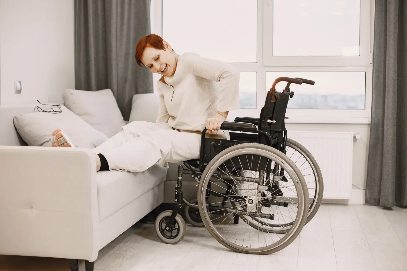 Seniorin mit Mobilitätseinschränkung wechselt zu Hause vom Rollstuhl auf das Sofa