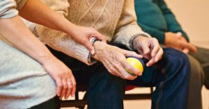An elderly person receives support from a caregiver, holding hands indoors, showcasing compassion.