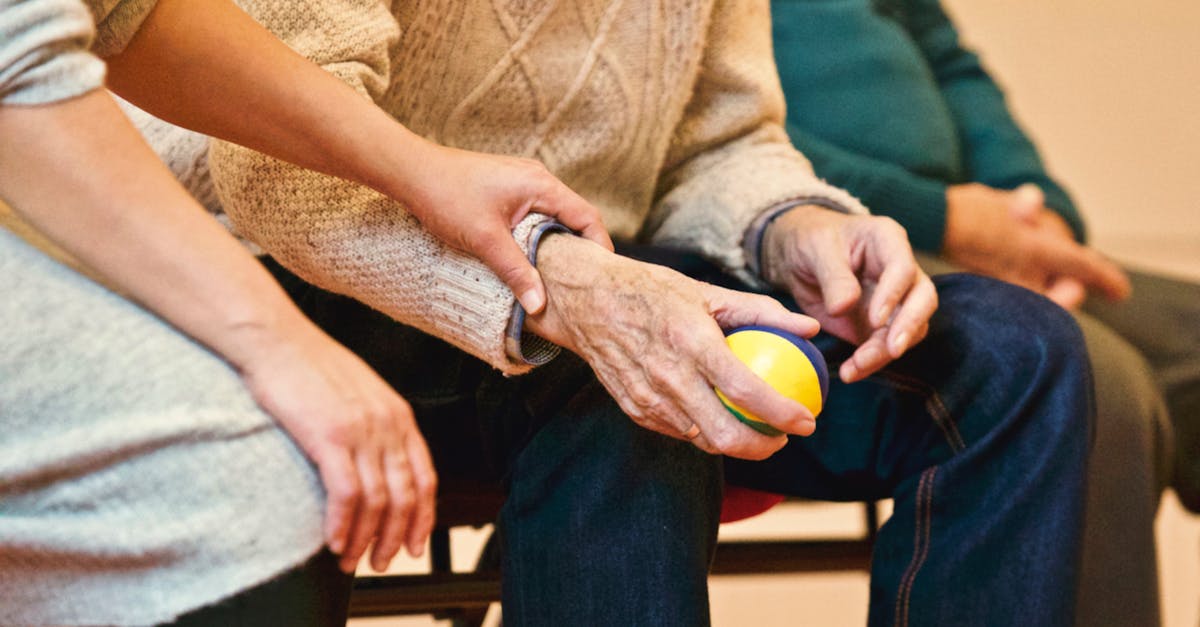 An elderly person receives support from a caregiver, holding hands indoors, showcasing compassion.