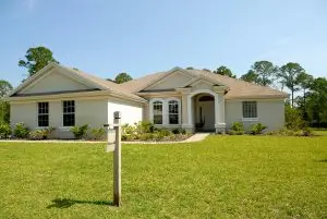 Beautiful suburban house with lush lawn, showcasing a for sale sign under a clear blue sky.
