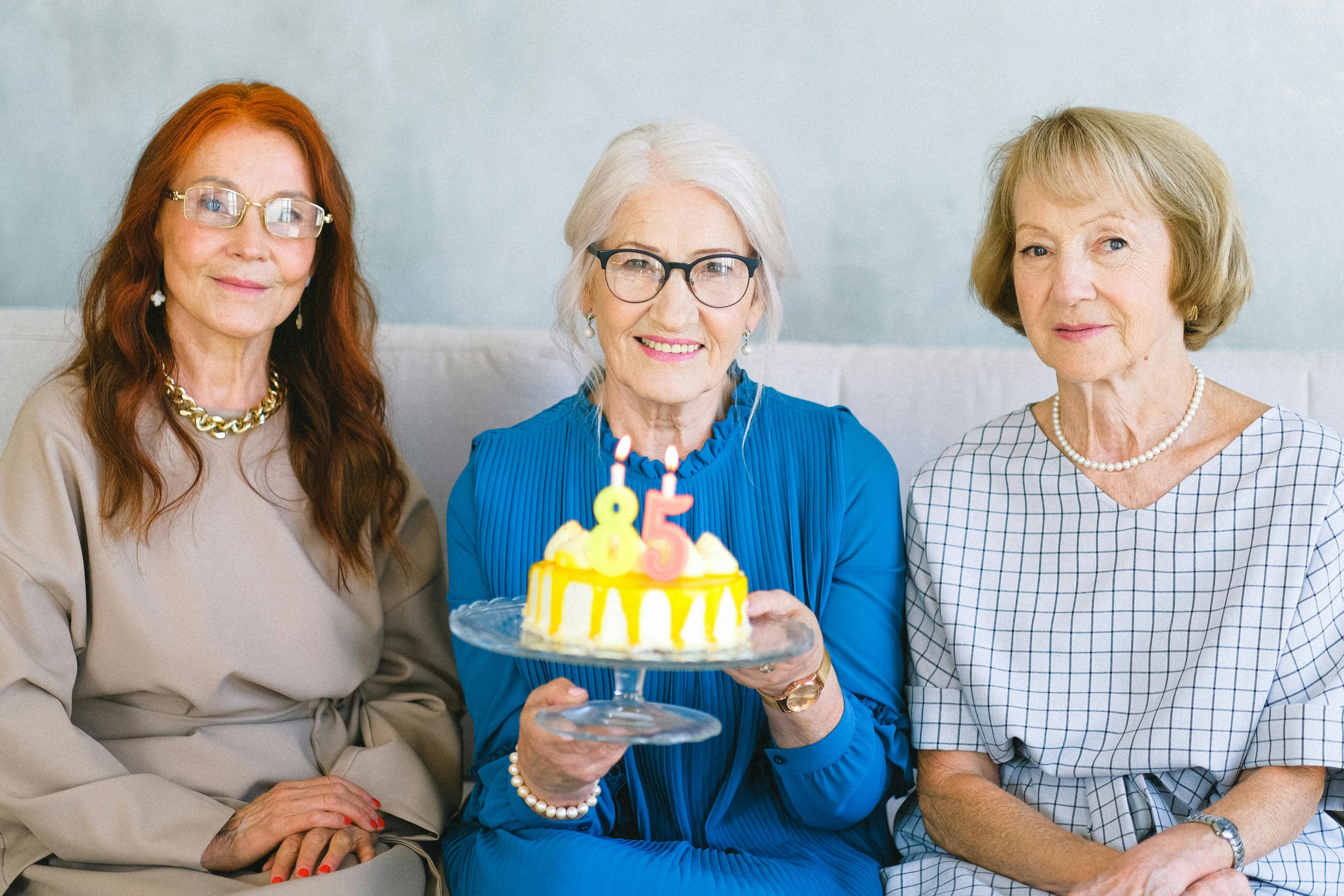 Three senior women joyfully celebrate an 85th birthday indoors with a cake.