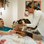 Seniorin sitzt zu Hause am Tisch und spricht mit einer Pflegekraft – Einsamkeit im Alter Frankfurt