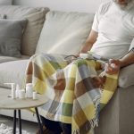 Elderly man monitoring blood pressure on a cozy couch at home, surrounded by medication.