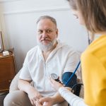 Senior sitzt nachts ruhig im Wohnzimmer während eine Pflegekraft unterstützend neben ihm steht – Nachtunruhe bei Senioren Frankfurt